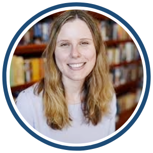  A circular headshot of a woman with long, wavy blonde hair, wearing a light-colored sweater. She has a warm smile and is positioned in front of bookshelves filled with books. The image is framed with a dark blue border.