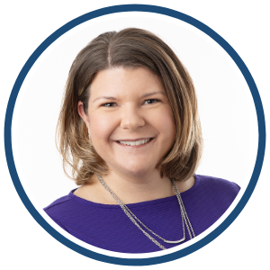 A circular headshot of a smiling woman with shoulder-length, light brown hair, wearing a purple top and layered silver necklaces. The background is a clean, white backdrop, and a dark blue border surrounds the image.